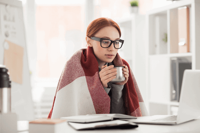 Woman sat at laptop with blanket and warm drink