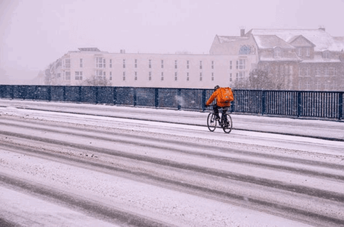 A delivery man with an orange back on a bicycle