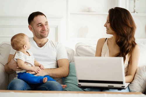 Couple sat with child on mans lap and woman on laptop