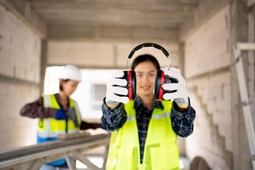 Employee holding ear defenders to protect against loud noise and noisy machines in accordance with noise regulations.