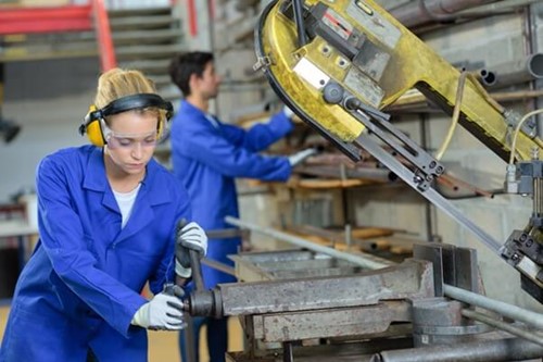 Employee operating machinery wearing ear defenders managing noise risks.