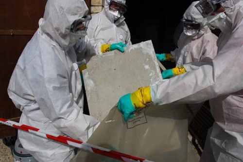 A team of asbestos contractors in ppe, removing crumbling asbestos boarding from a public building using proper disposal procedures.