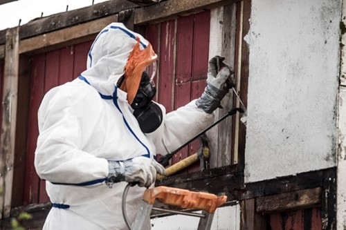 An asbestos contractor in respiratory gear, checks a dilapidated part of a building in an attempt to protect workers in line with correctly managing asbestos regulations.