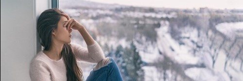 Female employee sat in a windowsill looking out at the wintery weather, feeling the effects of seasonal depression.