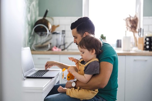Working father holding his child whilst working remotely.