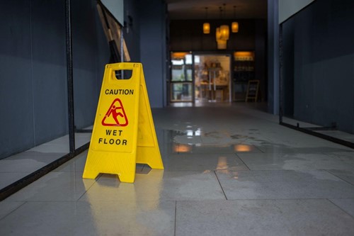A caution sign set up on a wet floor, to warn against slip hazards to help prevent slips trips and falls in the workplace.