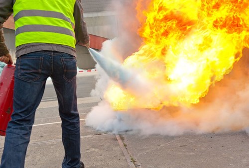 A person extinguishing a fire using a fire extinguisher under the correct fire safety control measures.