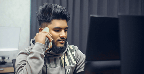 a man talking on phone whilst working on computer at desk