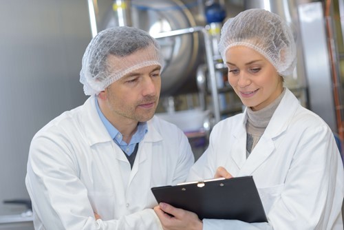 Two workers carrying out hazard analysis, and a food hygiene check to establish critical limits in the HACCP system.