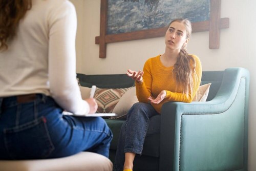Two women sitting on couch in consulting room talking about mental health issues