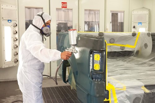Motor vehicle repair worker using respiratory PPE in alignment with COSSH regulations.